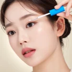 سرم تقویت مژه سپی‌پور Seapuri Lashrum با درپوش آبی، بدنه نقره‌ای و سفید و اپلیکاتور برس‌دار